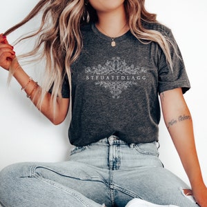May include: A dark grey t-shirt with a white floral design and the text "STFUATTDLAGG".