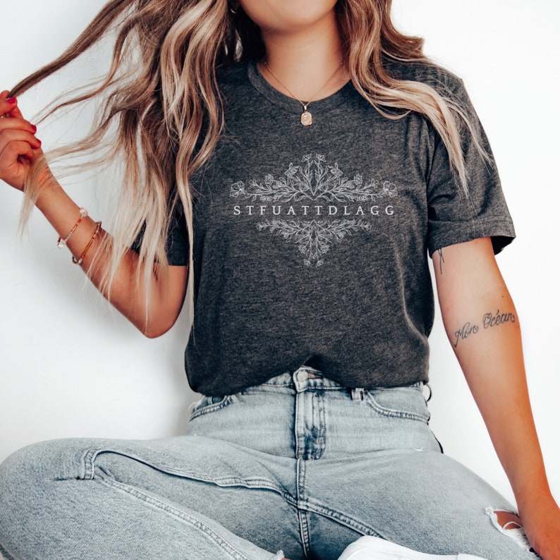 May include: A dark grey t-shirt with a white floral design and the text "STFUATTDLAGG".
