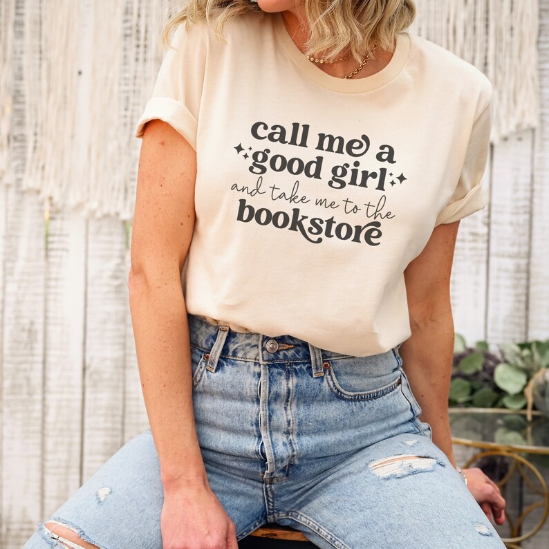 May include: A light beige t-shirt with the text "Call me a good girl and take me to the bookstore" in black.