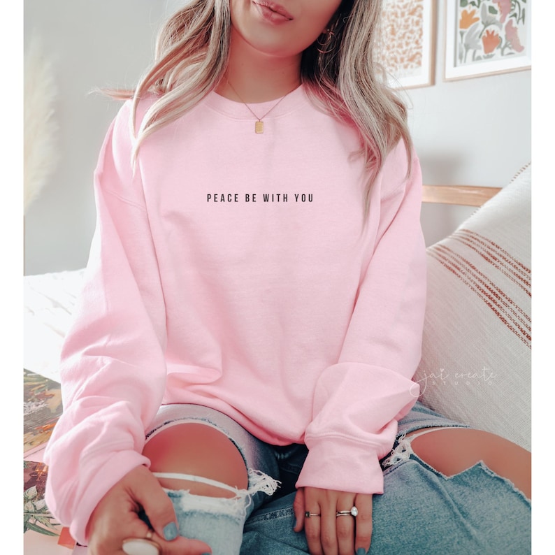 Pu&ograve; includere: Una felpa rosa con la scritta "Peace be with you" stampata sul davanti.
