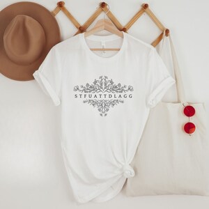 May include: White t-shirt with a floral design and the text "STFUATTDLAGG" printed on the front.