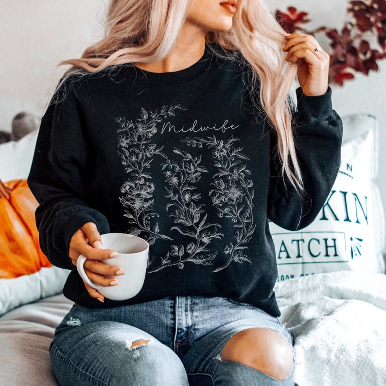 May include: Black sweatshirt with a white floral design and the word "Midwife" in white lettering.