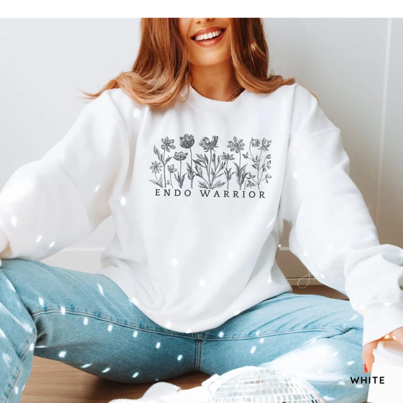 Pu&ograve; includere: Felpa bianca con un disegno floreale bianco e nero e il testo "ENDO WARRIOR".