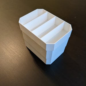 May include: White plastic organiser with three compartments. The organiser is stacked on top of itself, creating a taller container.