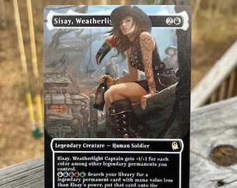May include: A black and white Magic: The Gathering card featuring a woman in a pirate hat with a toucan on her shoulder. The card is titled "Sisay, Weatherlight Captain" and has a power and toughness of 2/2. The card text reads: "Sisay, Weatherlight Captain gets +1/+1 for each colour among other legendary permanents you control. 00000: Search your library for a legendary permanent card with mana value less than Sisay's power, put that card onto the battlefield, then shuffle."