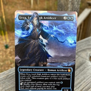 Puede incluir: Una carta de Magic: The Gathering con Urza, Lord High Artificer, una criatura legendaria con un esquema de color azul y blanco. La carta tiene un fondo negro con texto blanco y una ilustraci&oacute;n azul y blanca de Urza, un art&iacute;fice humano, sosteniendo un bast&oacute;n y un orbe brillante.