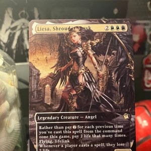 May include: A black and white Magic: The Gathering card featuring Liesa, Shroud of Dusk, a legendary creature - angel. The card has a black background with a detailed illustration of a woman with black wings and a golden crown. The card text reads "Rather than pay 2 for each previous time you've cast this spell from the command zone this game, pay 2 life that many times. Flying, lifelink. Whenever a player casts a spell, they lose 2 life."