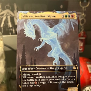 May include: A collectible trading card featuring "Miirym, Sentinel Wyrm," a Legendary Creature Dragon Spirit. The card has a blue and white ethereal dragon illustration against a dark background. The card's text includes game mechanics and a power/toughness of 6/6.