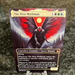 May include: A fantasy trading card featuring a creature called "The Wise Mothman". The card is illustrated with a dark, winged creature with glowing red eyes against a backdrop of a red and black sky. The card text describes the creature's abilities and stats.