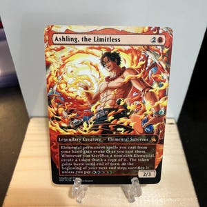 May include: A collectible card featuring the character Ashling, the Limitless, with a fiery background. The card has a red and orange color scheme, with text that reads "Legendary Creature - Elemental Sorcerer". The card is 2/3.
