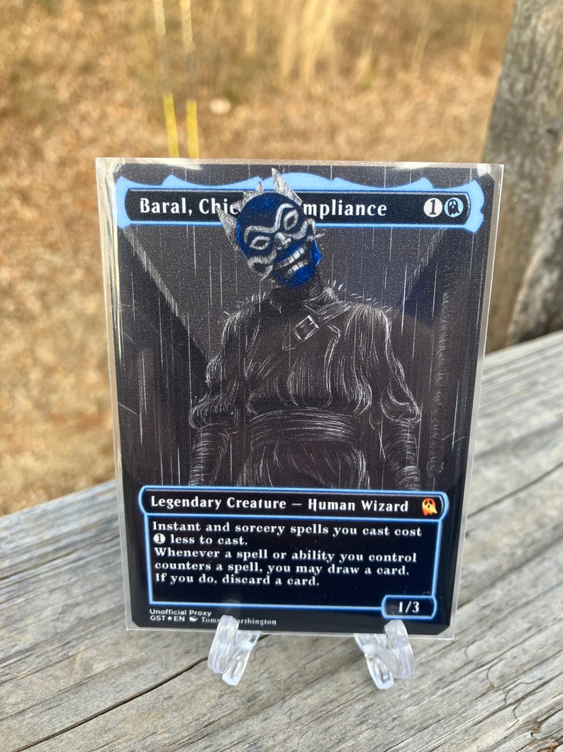 May include: A black and white Magic: The Gathering card with a blue and white illustration of a character with a mask. The card text reads "Baral, Chief of Compliance 1UU Legendary Creature - Human Wizard Instant and sorcery spells you cast cost less to cast. Whenever a spell or ability you control counters a spell, you may draw a card. If you do, discard a card. 1/3".