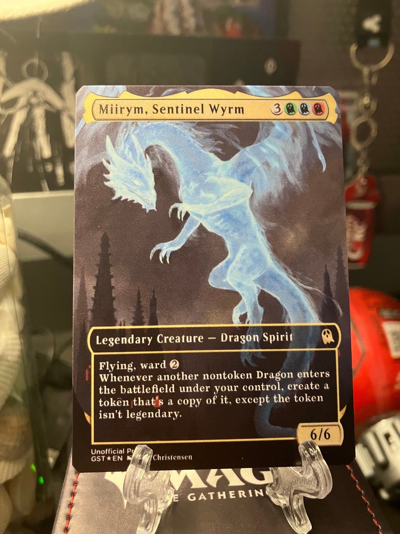May include: A collectible trading card featuring "Miirym, Sentinel Wyrm," a Legendary Creature Dragon Spirit. The card has a blue and white ethereal dragon illustration against a dark background. The card's text includes game mechanics and a power/toughness of 6/6.