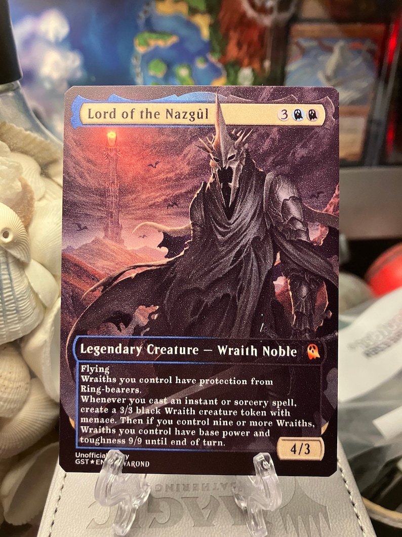 K&ouml;nnte beinhalten: Eine schwarz-wei&szlig;e Fantasy-Sammelkarte mit einer dunklen, schattenhaften Figur mit einem geh&ouml;rnten Helm. Die Karte tr&auml;gt den Titel "Lord of the Nazg&ucirc;l" und hat eine St&auml;rke und Widerstandsf&auml;higkeit von 4/3. Der Kartentext beschreibt die F&auml;higkeiten der Kreatur, darunter Fliegen und das Erschaffen von Wraith-Markern.