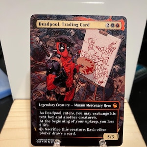May include: A trading card featuring Deadpool, a Marvel Comics superhero, in a red and black suit, holding a paintbrush and palette. He is painting a picture of himself and other characters on a canvas. The card is black with red and gold accents. The text on the card reads "Deadpool, Trading Card" and "Legendary Creature - Mutant Mercenary Hero".