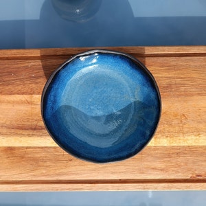 Peut inclure: Un bol en céramique bleu foncé avec un bord noir. Le bol est sur une surface en bois.