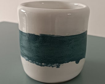 May include: White ceramic mug with a teal blue band around the middle.