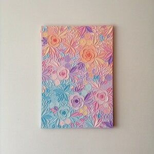 Puede incluir: Una obra de arte en lienzo rectangular con un dise&ntilde;o floral texturizado. La pieza utiliza una paleta de colores pastel de rosa, melocot&oacute;n, azul y morado. Las flores y las hojas est&aacute;n en relieve, creando un efecto tridimensional.