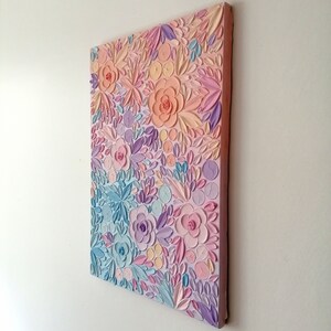 Puede incluir: Una obra de arte en lienzo rectangular con un dise&ntilde;o floral en relieve. La obra presenta colores pastel, incluyendo rosa, melocot&oacute;n, azul y lavanda. Las flores y hojas tienen textura, creando un efecto 3D. El lienzo est&aacute; montado sobre un marco de madera.