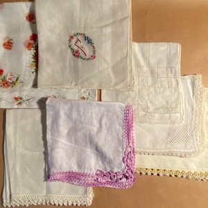 May include: Six white handkerchiefs with different embroidery designs. Some have lace trim. One has a floral design, one has a monogram, one has a checkered pattern, and one has a floral border.
