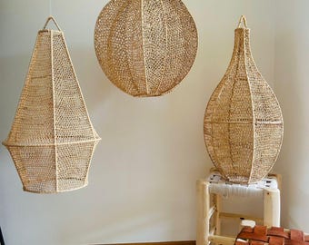 Peut inclure: Trois lampes suspendues en rotin tressé, une ronde, une conique et une en forme de vase, suspendues au plafond d'une pièce aux murs blancs et un tapis blanc avec des accents orange et violet.