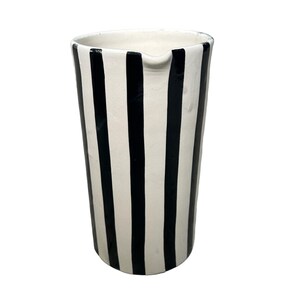 May include: A white ceramic pitcher with black vertical stripes. The pitcher has a wide mouth and a handle.