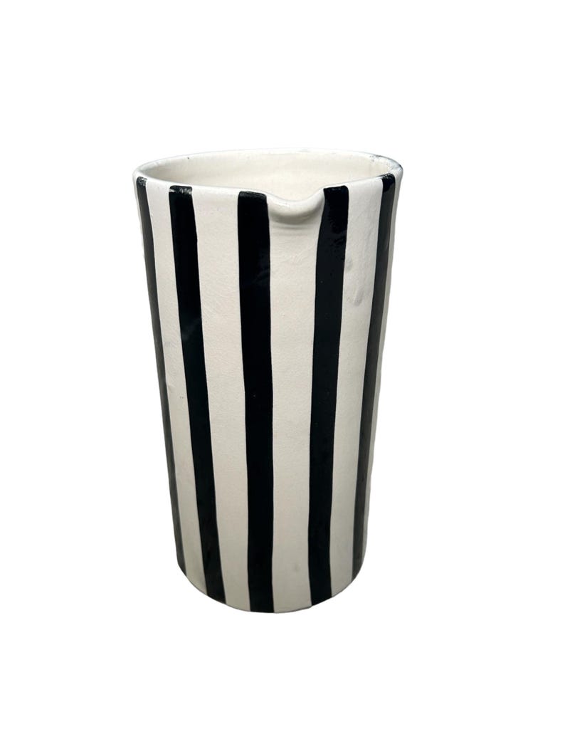 May include: A white ceramic pitcher with black vertical stripes. The pitcher has a wide mouth and a handle.