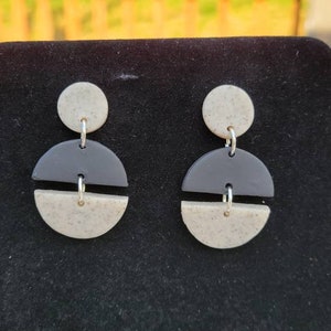 May include: A pair of black and white geometric earrings. The earrings are made of two circles, one black and one white, with a small silver ring connecting them.