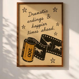 Könnte beinhalten: Gerahmter Kunstdruck im Vintage-Stil. Das Kunstwerk zeigt eine Filmrolle und einen Filmstreifen mit Pferdesilhouetten, zusammen mit dem Text "Dramatic endings & happier times ahead." Der Druck ist in einem braunen Holzrahmen.