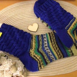 Könnte beinhalten: Ein Paar gestrickte Socken in blau-grünen Streifen mit einer blauen Rippenstrick-Manschette. Die Socken liegen auf einer geflochtenen Strohmatte.