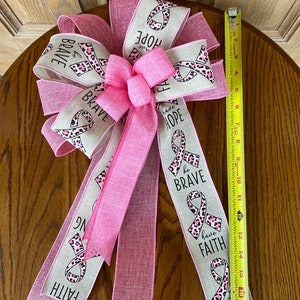 May include: A pink and beige ribbon bow with a pink leopard print and the words "be brave", "have faith", and "have hope".