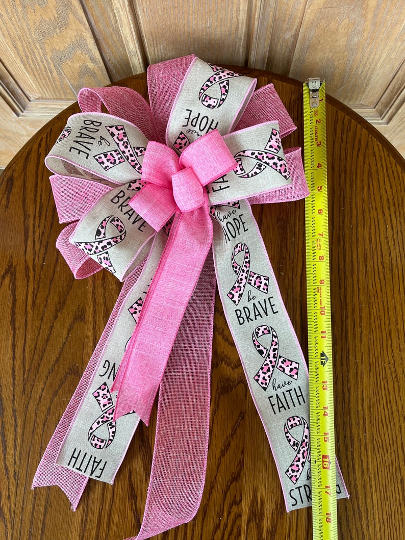 May include: A pink and beige ribbon bow with a pink leopard print and the words "be brave", "have faith", and "have hope".