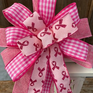 May include: A pink and white gingham ribbon bow with a pink ribbon printed with pink glitter ribbon designs. The bow is tied around a white lantern.