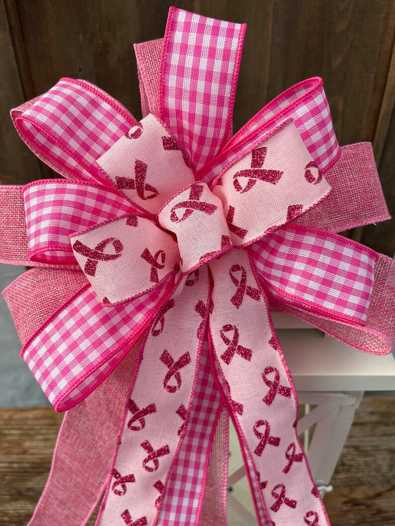 May include: A pink and white gingham ribbon bow with a pink ribbon printed with pink glitter ribbon designs. The bow is tied around a white lantern.