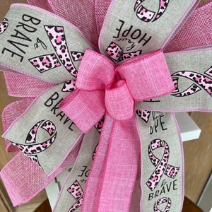 May include: Pink and beige ribbon with a pink leopard print and the words "Be Brave", "Hope", "Be Strong", "Be Brave", and "Faith" printed on it.