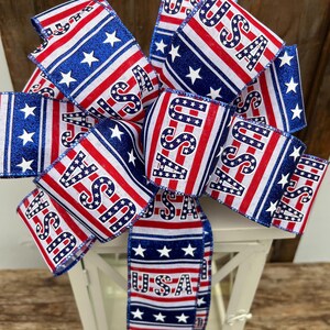 May include: A red, white, and blue ribbon bow with the word "USA" printed on it. The bow is tied around a white lantern.