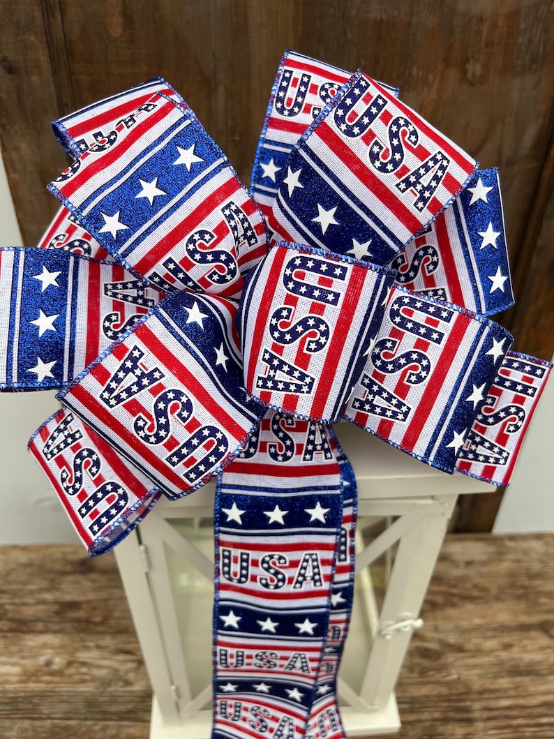 May include: A red, white, and blue ribbon bow with the word "USA" printed on it. The bow is tied around a white lantern.