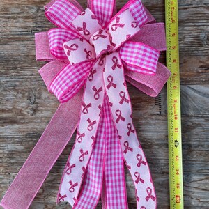 May include: A pink and white gingham ribbon bow with pink ribbon streamers featuring pink glitter ribbon bows. The streamers are tied together in the center with a pink ribbon bow.