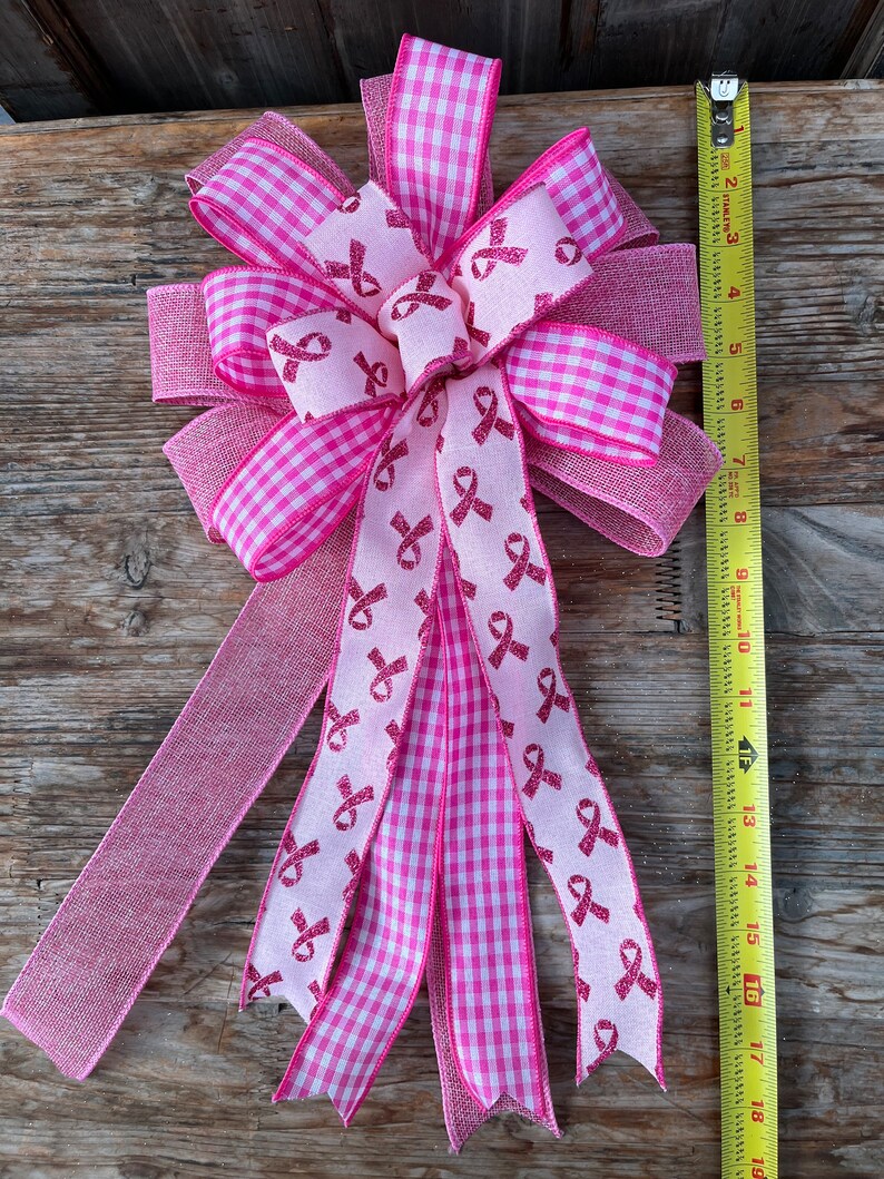 May include: A pink and white gingham ribbon bow with pink ribbon streamers featuring pink glitter ribbon bows. The streamers are tied together in the center with a pink ribbon bow.