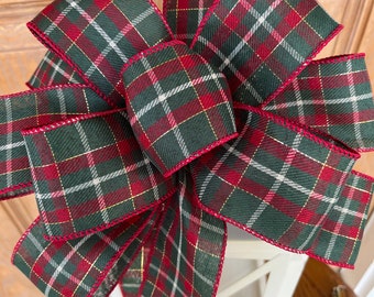 May include: A large plaid bow with red, green, white, and gold accents. The bow is made of a woven fabric with a wired edge.