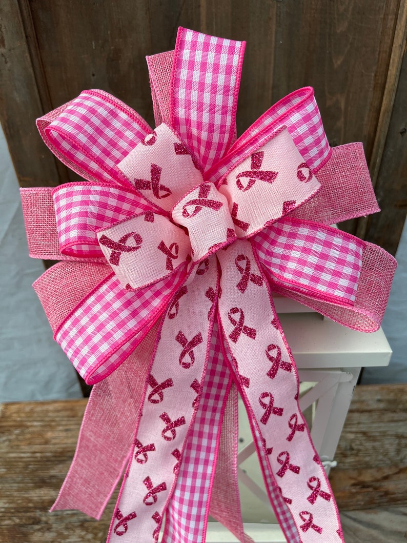 May include: Pink and white gingham ribbon bow with a pink ribbon tail featuring a pink glitter ribbon design of multiple pink ribbons.
