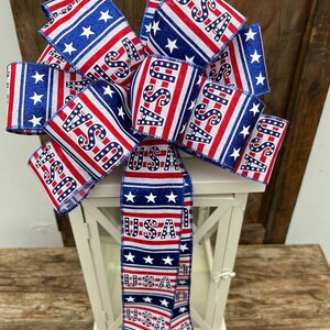 May include: A red, white, and blue bow with stars and the word "USA" printed on it. The bow is tied around a white lantern.