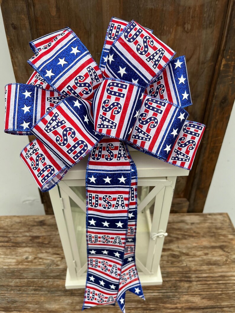 May include: A red, white, and blue bow with stars and the word "USA" printed on it. The bow is tied around a white lantern.