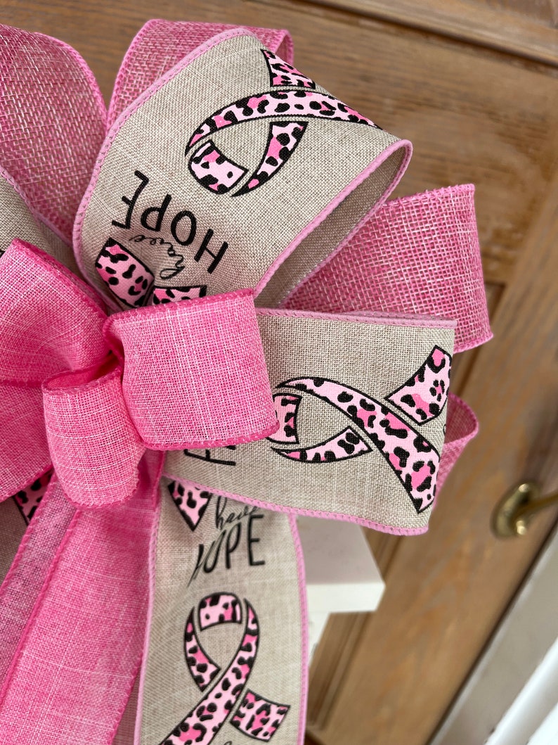 May include: Pink and brown ribbon with a leopard print design and the words "Have Hope" on a burlap background.