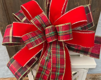 May include: A red velvet and plaid Christmas bow with gold trim. The bow is tied around a white lantern.