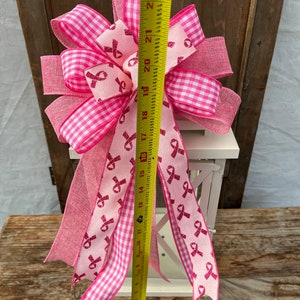 May include: A pink and white gingham ribbon bow with pink glitter ribbon accents. The bow is tied around a white lantern. The bow is approximately 18 inches tall.
