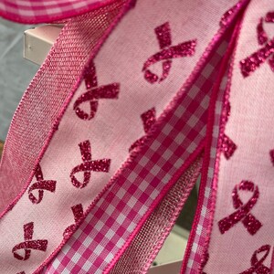 May include: Pink ribbon patterned ribbon with pink and white gingham ribbon and pink mesh ribbon. The ribbons are all tied together in a bow.