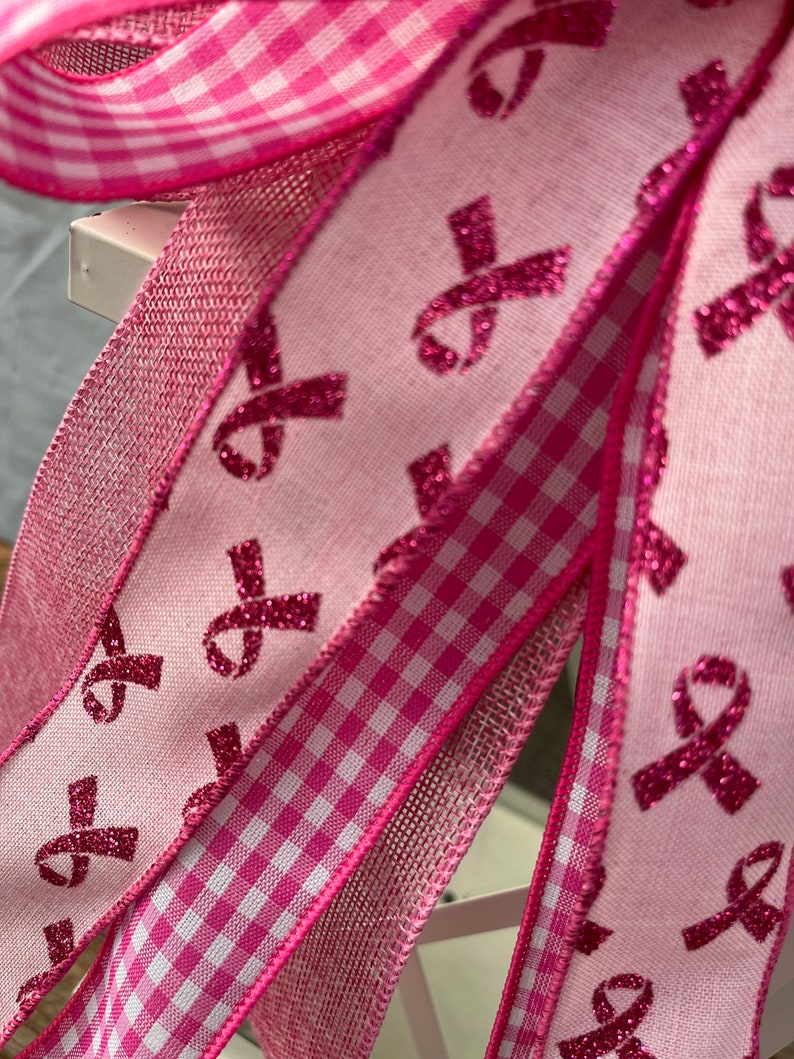 May include: Pink ribbon patterned ribbon with pink and white gingham ribbon and pink mesh ribbon. The ribbons are all tied together in a bow.