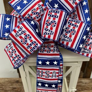 May include: A red, white, and blue ribbon bow with the word "USA" printed on it. The bow is tied around a white lantern.