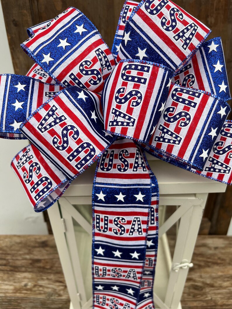 May include: A red, white, and blue ribbon bow with the word "USA" printed on it. The bow is tied around a white lantern.