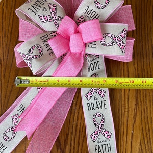 May include: A pink and beige ribbon bow with a leopard print and the words "be brave", "have hope", and "have faith".